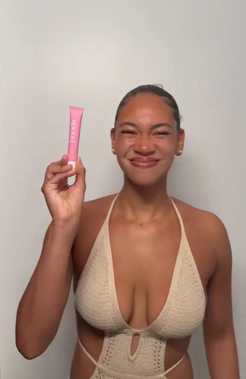 Femme souriante tenant une colle corporelle rose résistante à l'eau et à la transpiration pour maintenir les vêtements en place